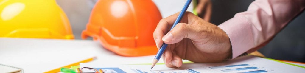 Een pen in een hand met op de achtergrond een bouwhelm