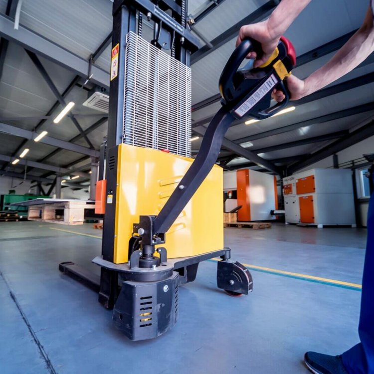 A worker in a warehouse uses a hand pallet stacker to transport pallets.